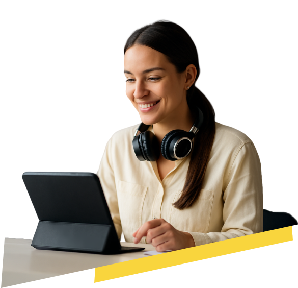 Mujer joven de cabello castaño recogido en coleta baja, sonriendo mientras trabaja en una tablet negra. Viste una camisa beige clara y lleva audífonos de diadema negros alrededor del cuello. Está sentada en un escritorio, en un entorno iluminado suavemente.