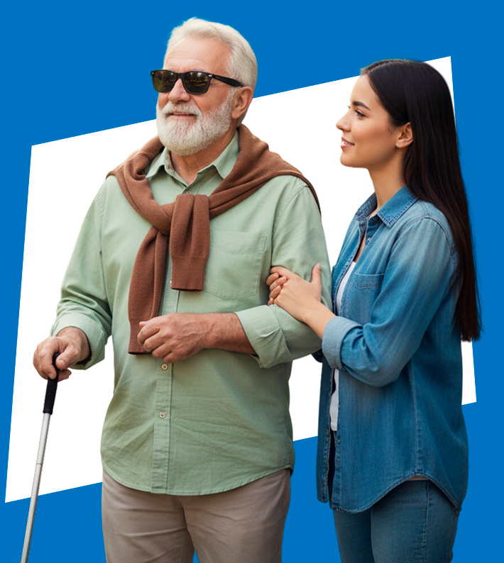 Una joven mujer sonr&iacute;e mientras sostiene el brazo de un hombre mayor ciego, quien sostiene un bast&oacute;n blanco. El hombre lleva gafas oscuras, una camisa verde y un su&eacute;ter marr&oacute;n sobre los hombros.